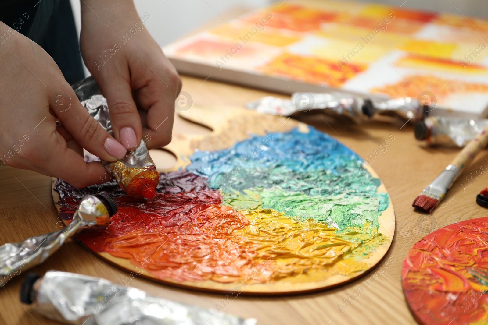 Photo of Woman squeezing paint from tube onto on palette at wooden table, closeup