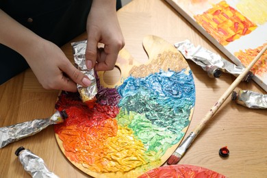 Photo of Woman squeezing paint from tube onto on palette at wooden table, above view