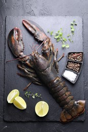 Photo of Raw lobster, cut lime, microgreens and spices on dark textured table, top view