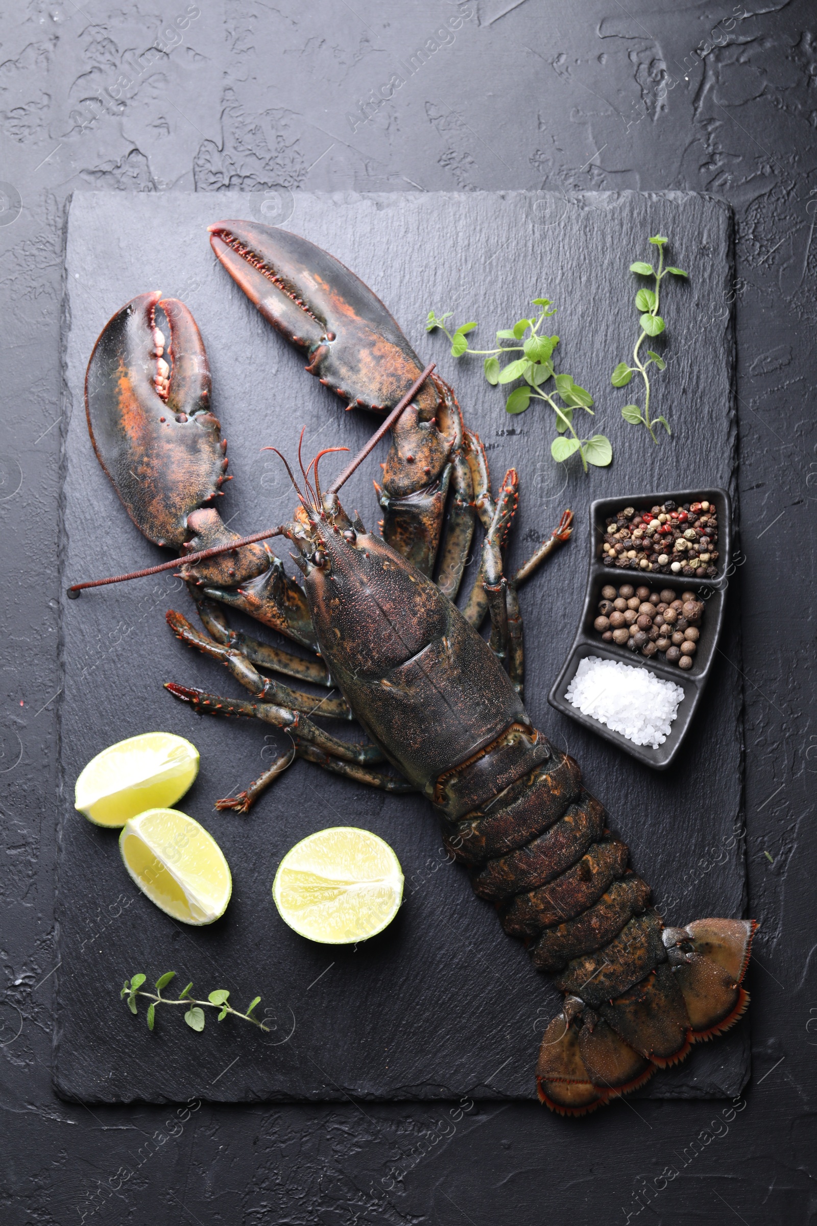 Photo of Raw lobster, cut lime, microgreens and spices on dark textured table, top view