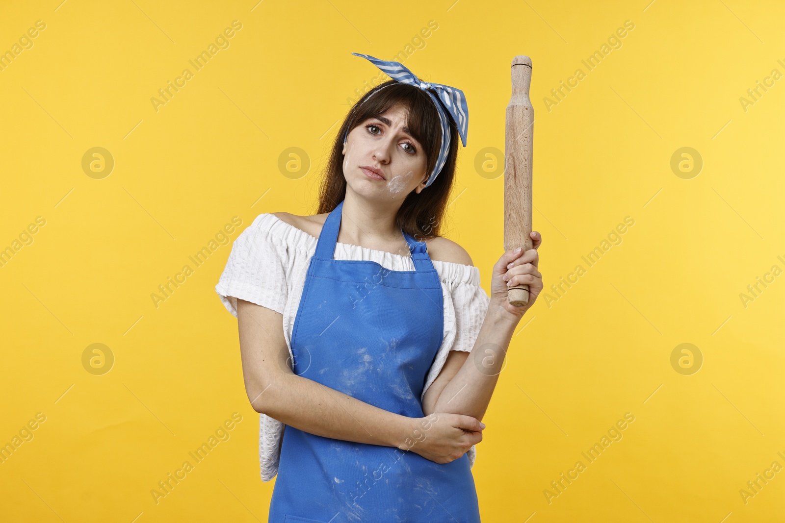 Photo of Upset woman with rolling pin on yellow background