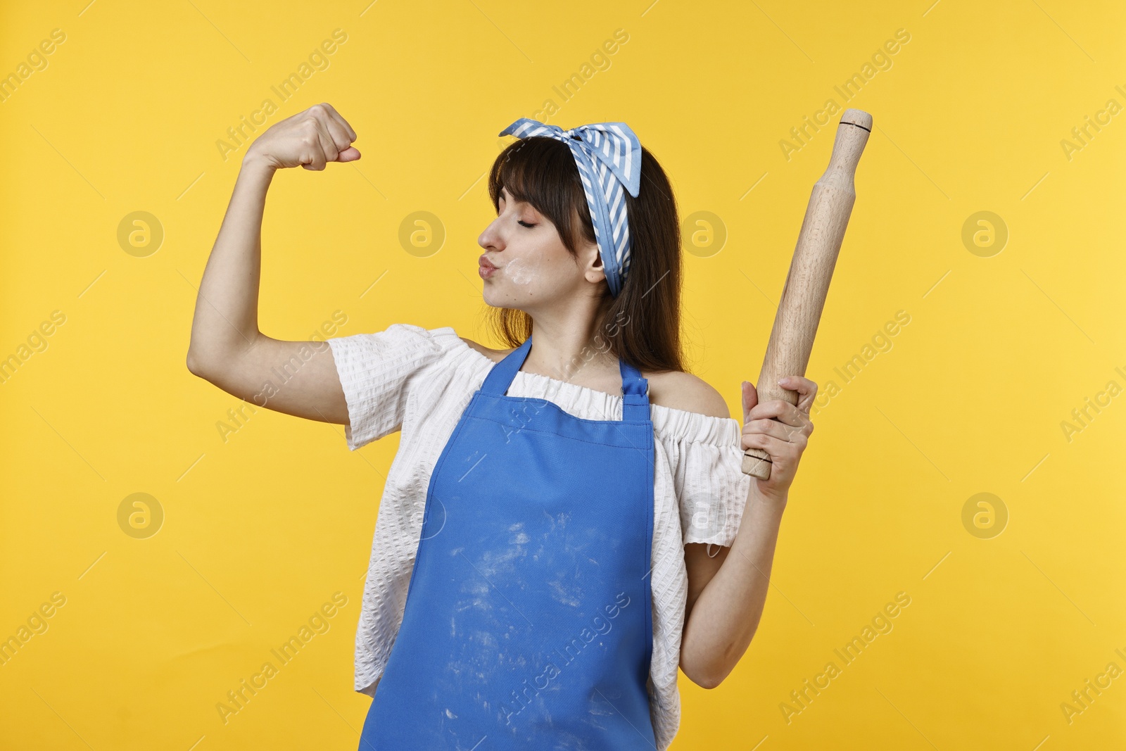 Photo of Woman with rolling pin kissing bicep on yellow background