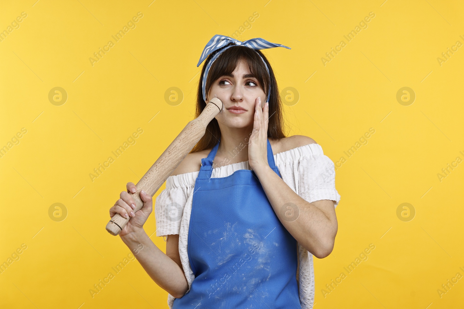 Photo of Pensive woman with rolling pin on yellow background