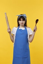 Photo of Angry woman with rolling pin and spoon on yellow background