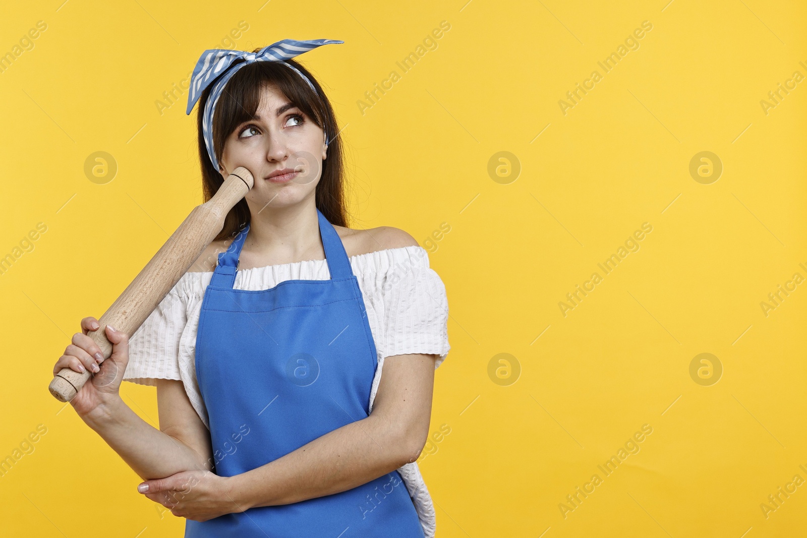 Photo of Pensive woman with rolling pin on yellow background. Space for text