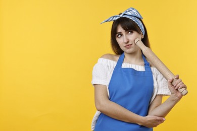 Photo of Pensive woman with rolling pin on yellow background. Space for text