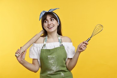 Photo of Happy woman with rolling pin and whisk on yellow background