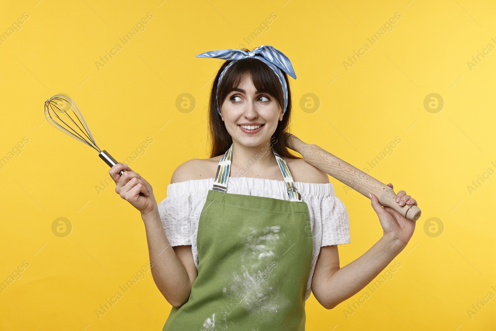 Photo of Happy woman with rolling pin and whisk on yellow background