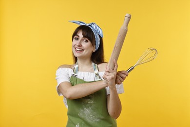 Photo of Happy woman with rolling pin and whisk on yellow background