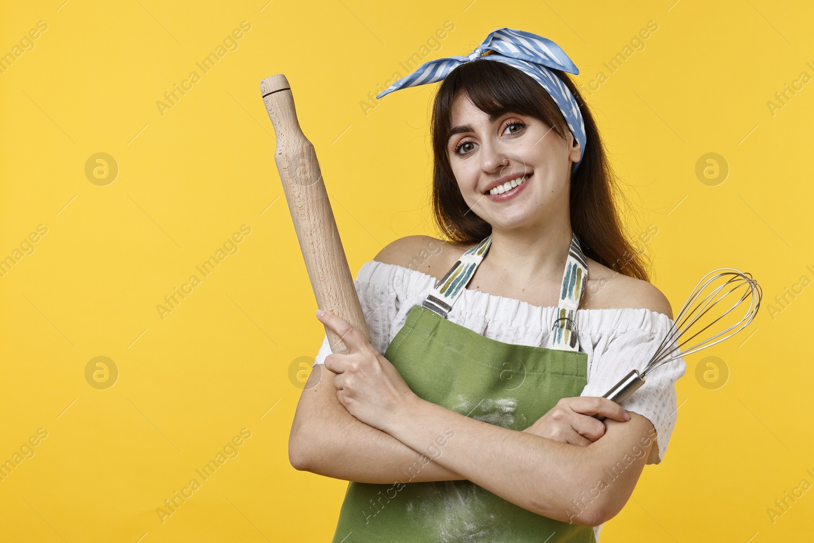 Photo of Happy woman with rolling pin and whisk on yellow background