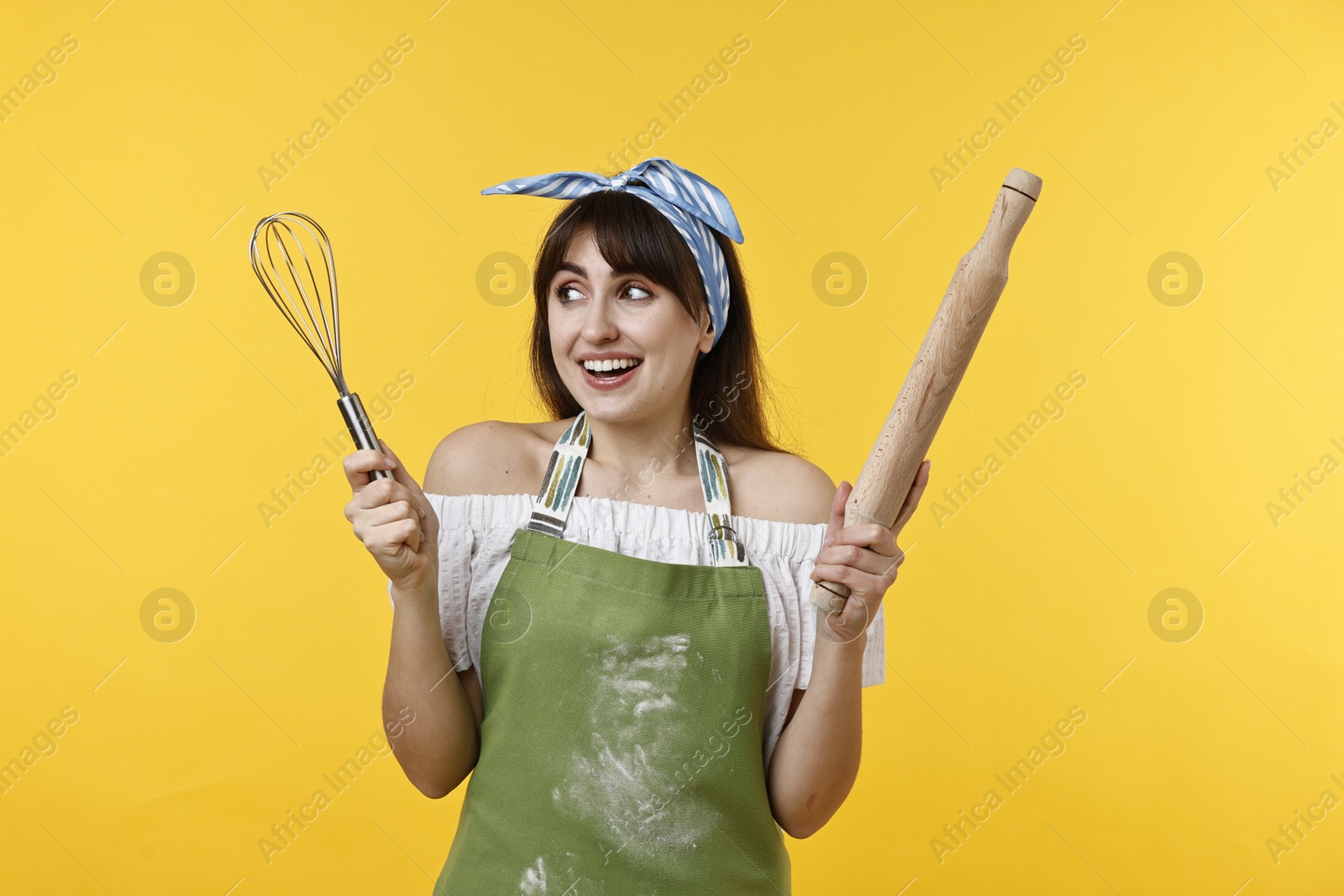 Photo of Happy woman with rolling pin and whisk on yellow background