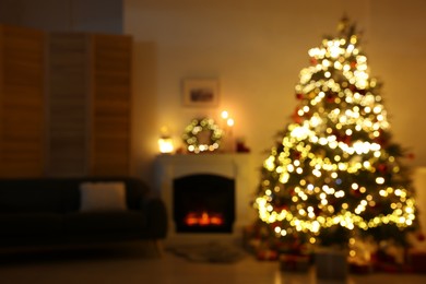 Photo of Blurred view of decorated Christmas tree near fireplace in room. Festive interior design