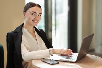 Photo of Woman in stylish formal suit working on laptop at table indoors