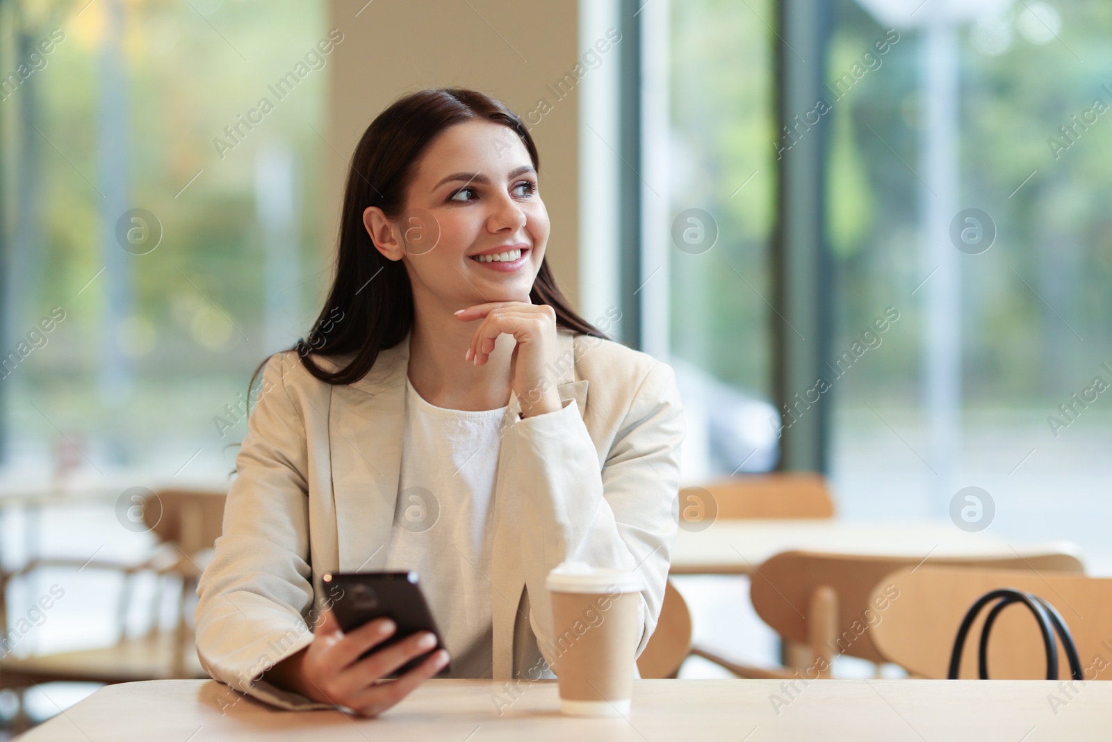 Photo of Woman in stylish formal suit with phone and coffee at table indoors