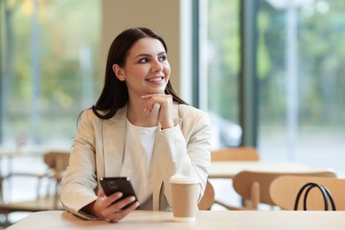 Photo of Woman in stylish formal suit with phone and coffee at table indoors