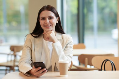 Photo of Woman in stylish formal suit with phone and coffee at table indoors