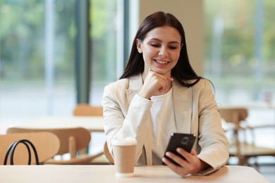 Photo of Woman in stylish formal suit with phone and coffee at table indoors