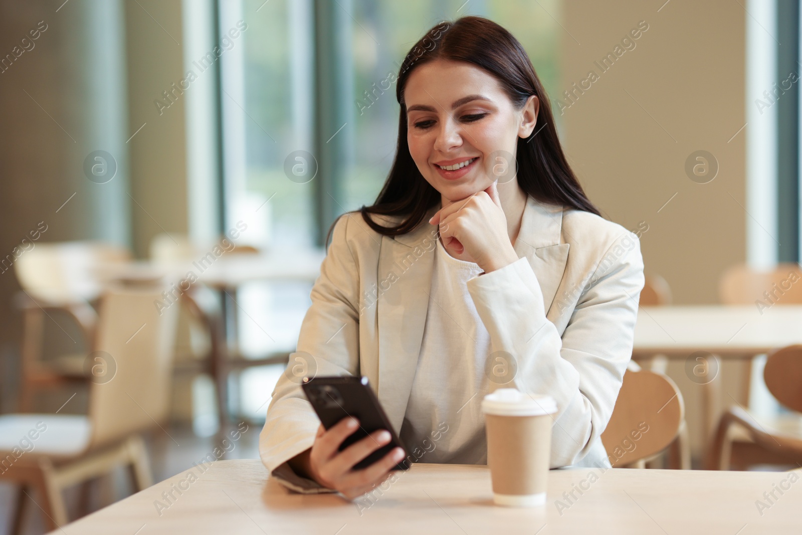 Photo of Woman in stylish formal suit with phone and coffee at table indoors