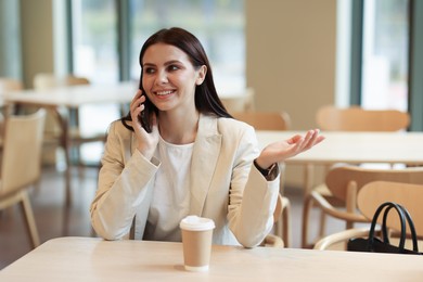 Photo of Woman in stylish formal suit talking on phone indoors