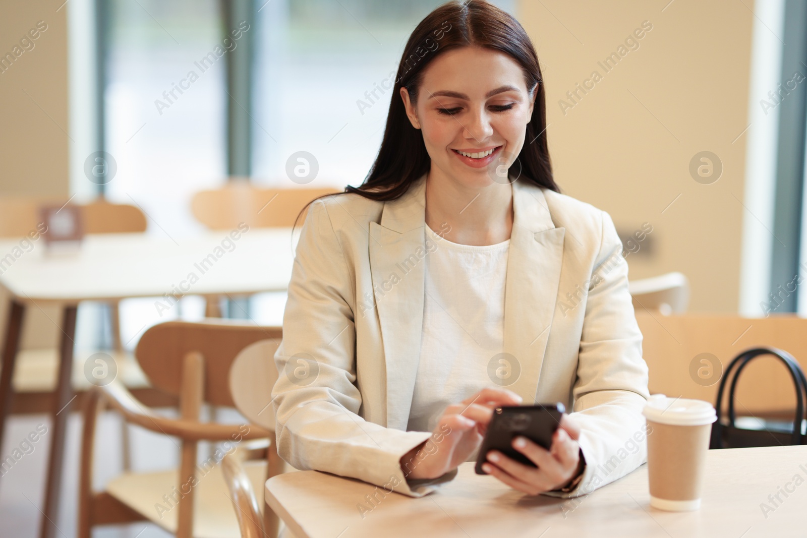 Photo of Woman in stylish formal suit with phone and coffee at table indoors