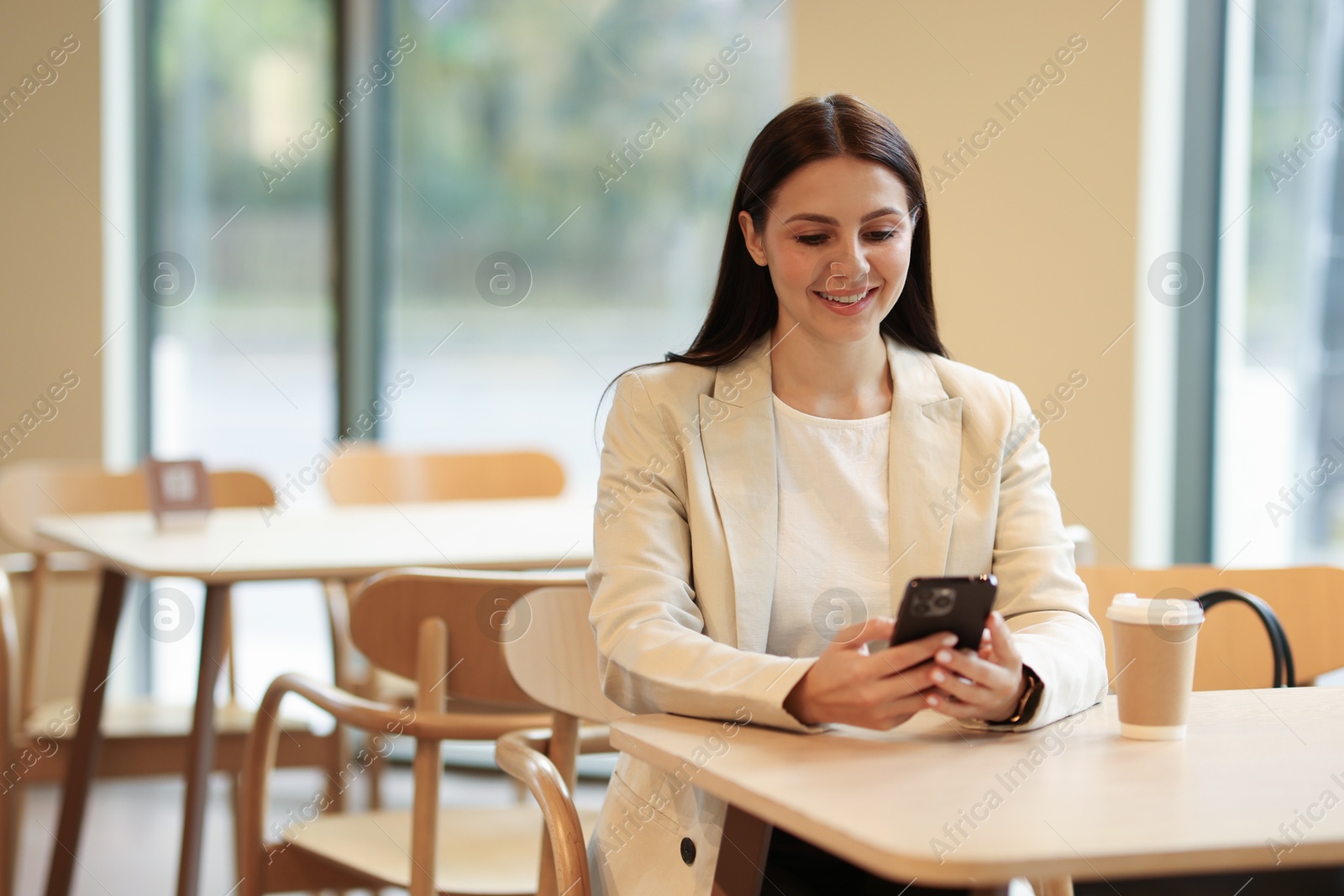 Photo of Woman in stylish formal suit with phone and coffee at table indoors. Space for text