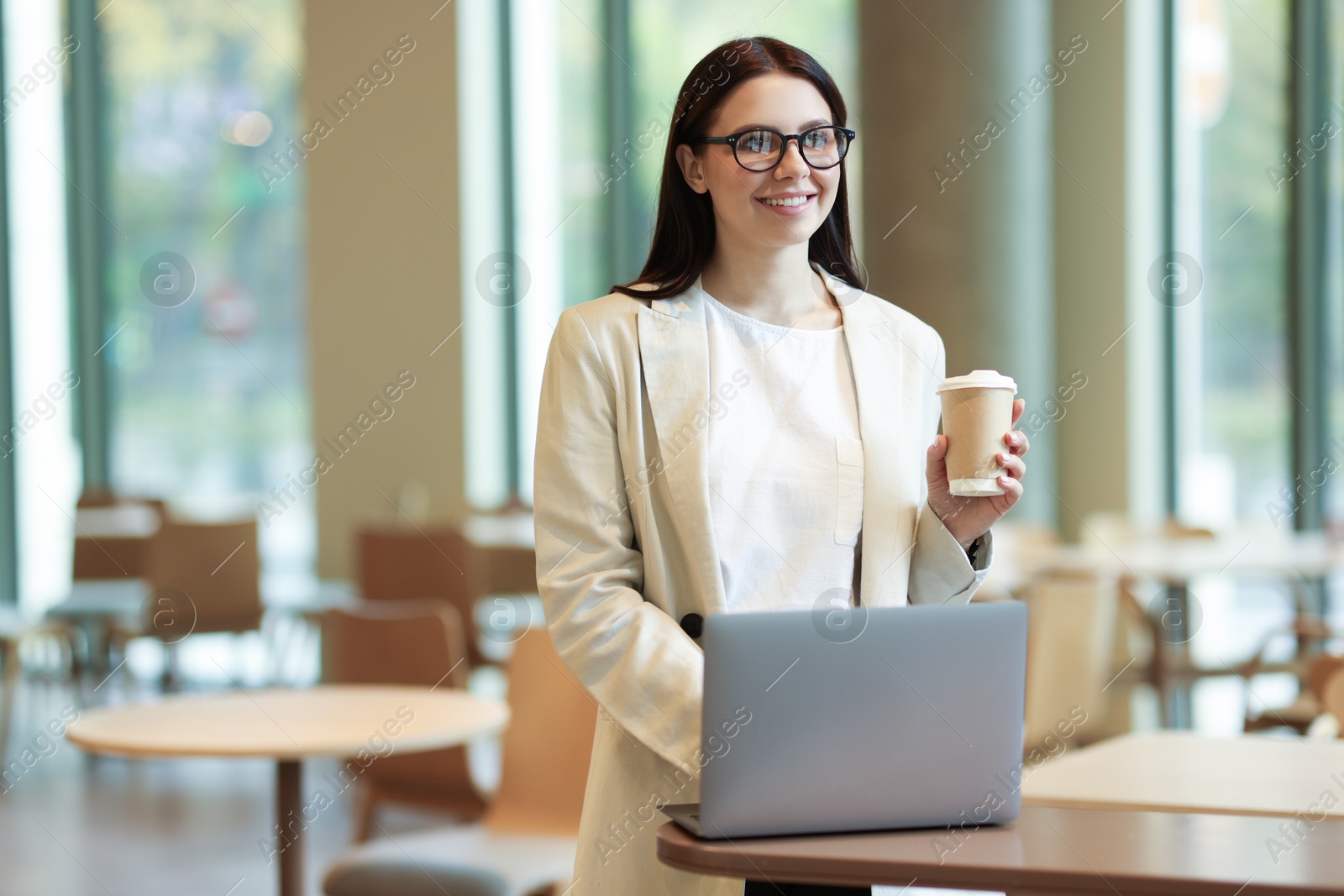 Photo of Woman in stylish formal suit with coffee working on laptop indoors