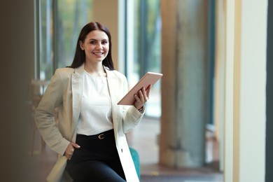 Photo of Woman in stylish formal suit with tablet indoors. Space for text