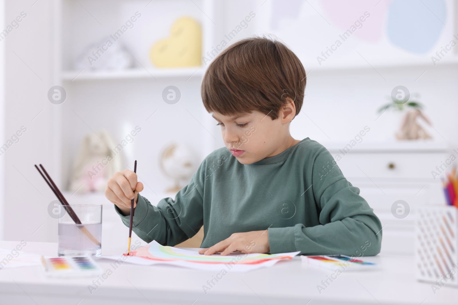 Photo of Cute boy drawing at white table in kindergarten