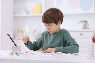 Photo of Cute boy drawing at white table in kindergarten