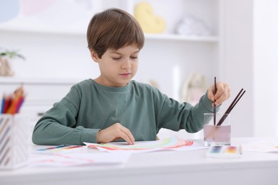 Photo of Cute boy drawing at white table in kindergarten