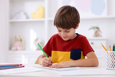 Photo of Cute boy drawing at white table in kindergarten