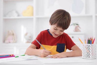 Photo of Cute boy drawing at white table in kindergarten