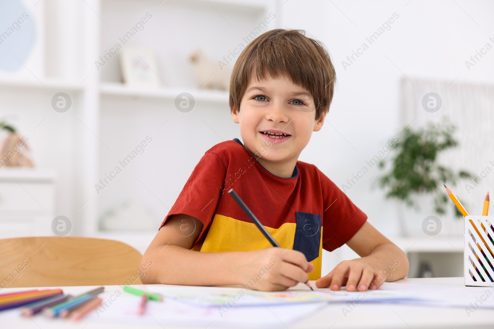 Photo of Happy boy drawing at white table in kindergarten