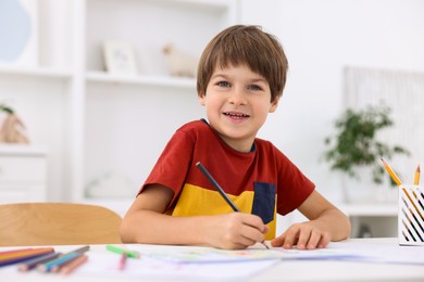 Photo of Happy boy drawing at white table in kindergarten