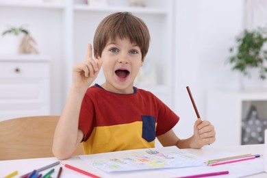 Photo of Emotional boy had idea for his drawing at white table in kindergarten