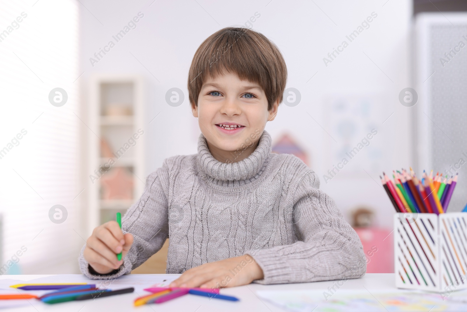 Photo of Happy boy drawing at white table in kindergarten