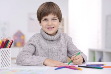 Photo of Happy boy drawing at white table in kindergarten