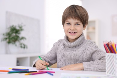 Photo of Happy boy drawing at white table in kindergarten