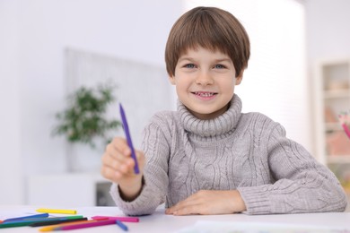 Photo of Happy boy drawing at white table in kindergarten