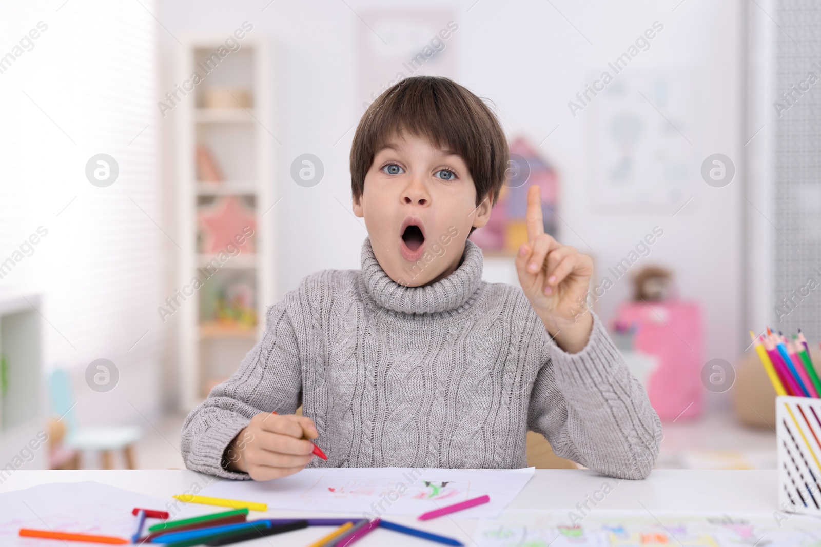 Photo of Emotional boy had idea for his drawing at white table in kindergarten