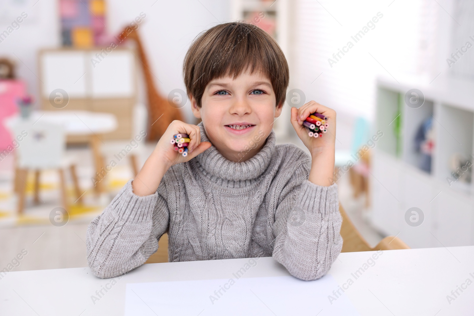 Photo of Portrait of smiling boy with colorful pencils at white table in kindergarten