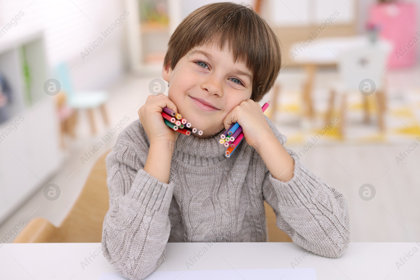 Photo of Portrait of cute boy with colorful pencils at white table in kindergarten