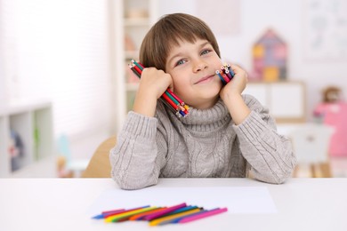 Photo of Portrait of cute boy with colorful pencils at white table in kindergarten