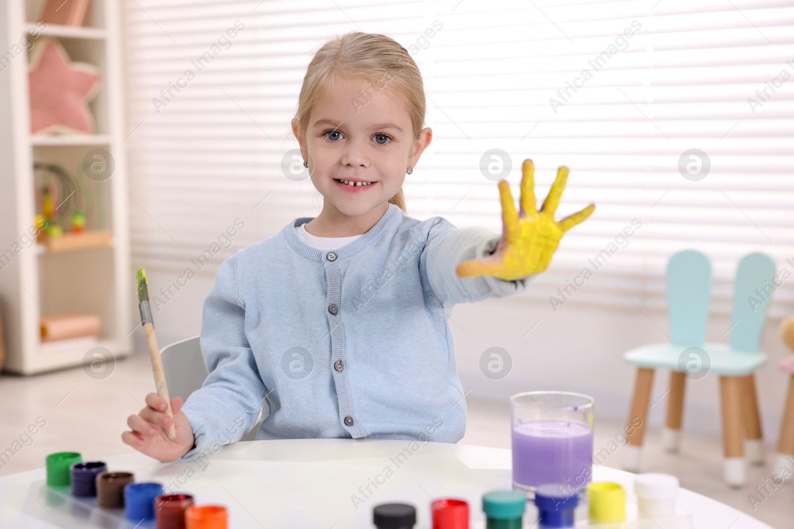 Photo of Happy girl drawing with palm at white table in kindergarten