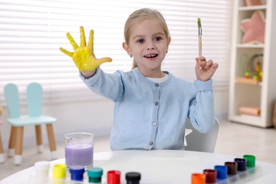 Photo of Happy girl drawing with palm at white table in kindergarten