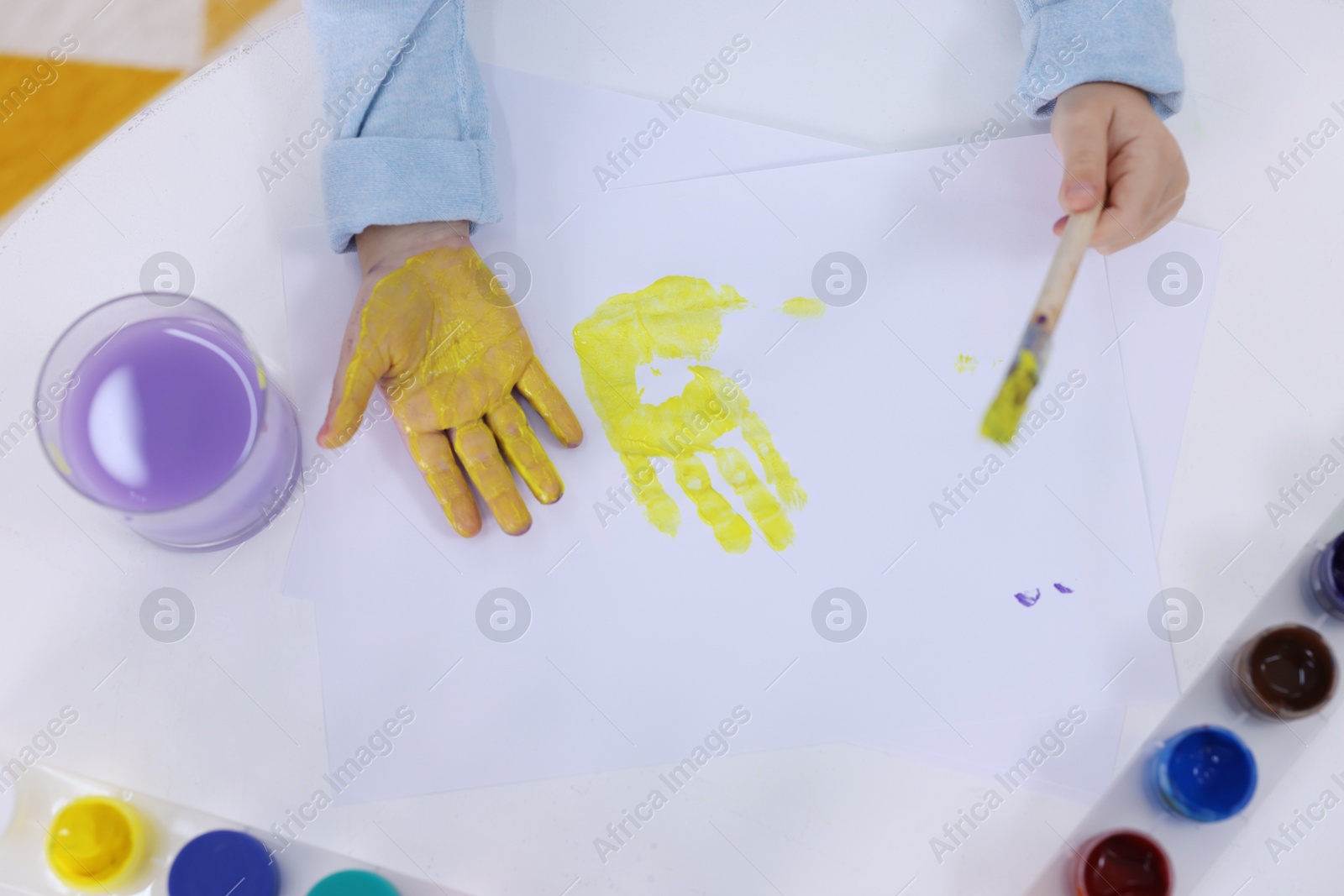 Photo of Girl drawing with palm at white table indoors, top view