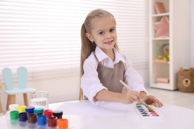 Photo of Smiling girl drawing at white table in kindergarten