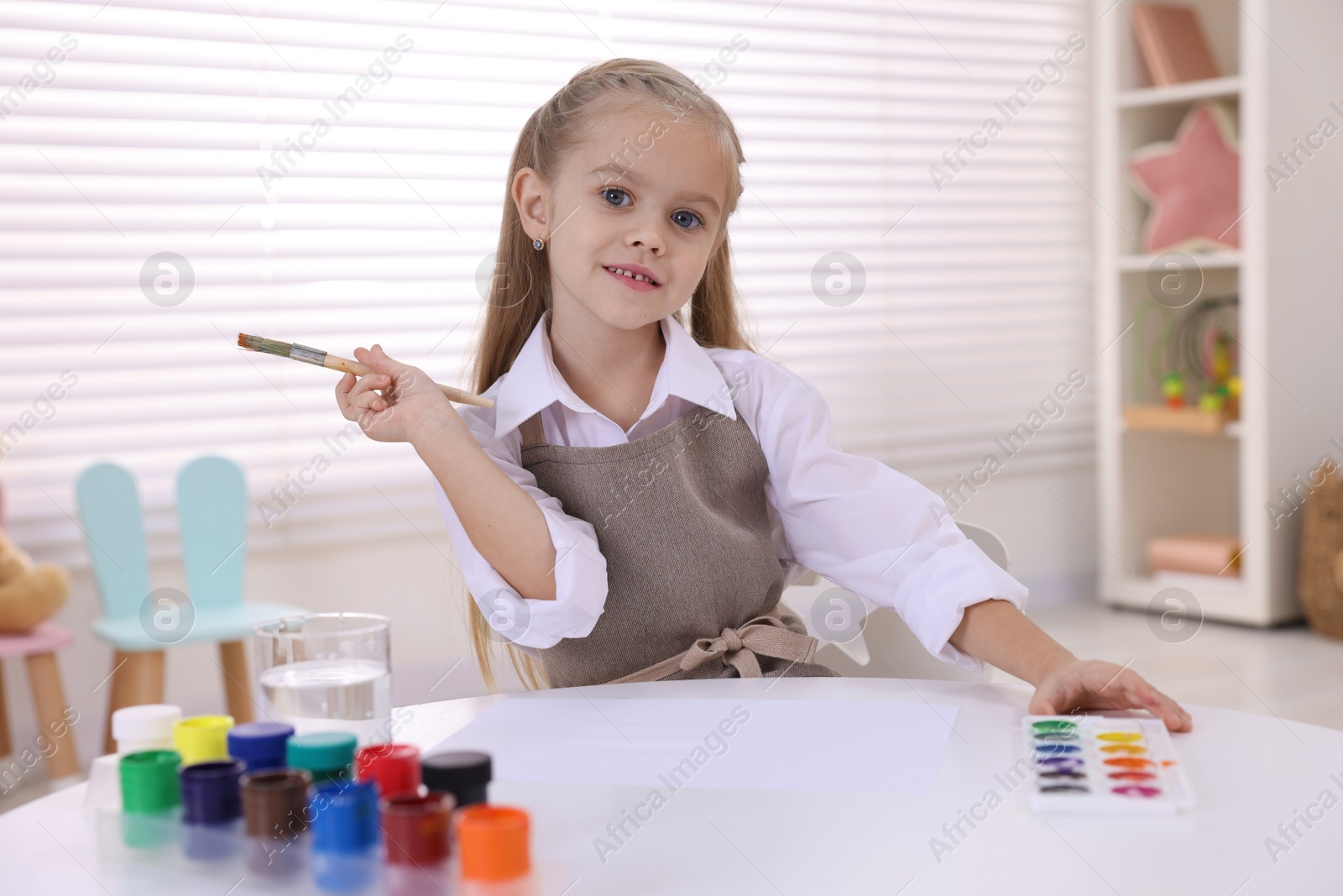 Photo of Smiling girl drawing at white table in kindergarten