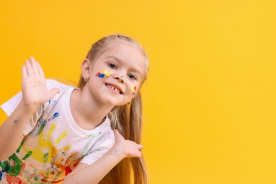 Photo of Portrait of smiling girl smeared in paint on orange background. Space for text