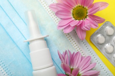 Photo of Allergy treatment. Nasal spray, pills, protective mask and flowers on yellow background, flat lay